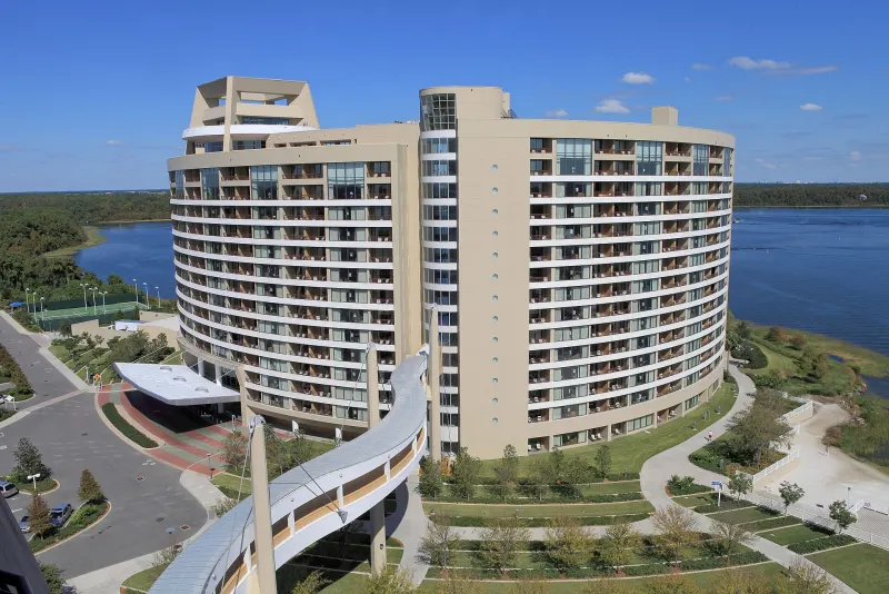Bay Lake Tower's curved high-rise beside Bay Lake, seen from above with the walkway bridge to the Contemporary Resort
