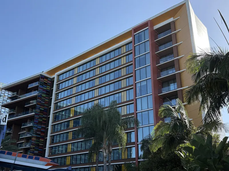 A Disneyland Hotel tower with balconies and colorful vertical accents, framed by palm trees under a blue sky
