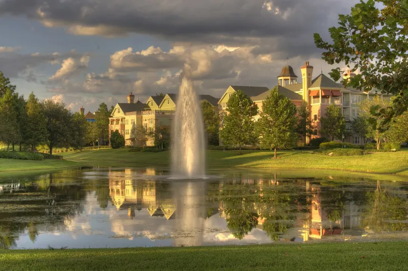 Saratoga Springs' Victorian-style buildings behind a pond with a tall fountain, under a dramatic cloudy sky