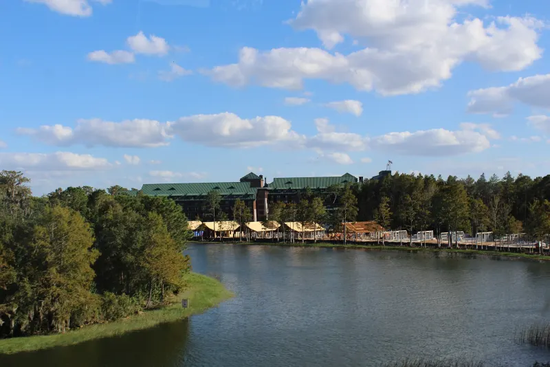 Disney's Wilderness Lodge rising above the pine forest across Bay Lake under a blue sky with white clouds